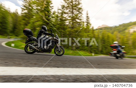 Touring motorcycle rider navigating a winding mountain road through forest scenery. Motion blur and dynamic perspective emphasize travel, adventure and freedom on two wheels. Touring motorcycle rider navigating a winding mountain road through forest scenery. Motion blur and dynamic perspective emphasize travel, adventure and freedom on two wheels. 140704736