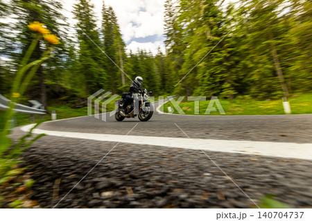 Touring motorcycle rider navigating a winding mountain road through forest scenery. Motion blur and dynamic perspective emphasize travel, adventure and freedom on two wheels. Touring motorcycle rider navigating a winding mountain road through forest scenery. Motion blur and dynamic perspective emphasize travel, adventure and freedom on two wheels. 140704737