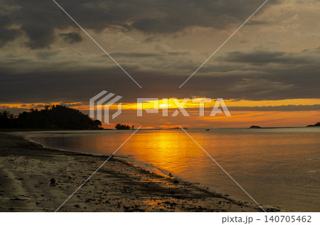 Golden sunset reflecting across still coastal waters with dramatic clouds enhancing the scenic shoreline view 140705462