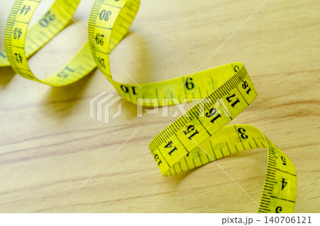 Yellow measuring tape arranged on a wooden surface representing fitness progress measurement 140706121