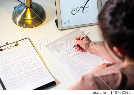 Quiet scene of woman writing with pen. Training accurate handwriting. Therapeutic habit to reduce anxiety and increase clarity. Calmness and digital detox Quiet scene of woman writing with pen. Training accurate handwriting. Therapeutic habit to reduce anxiety and increase clarity. Calmness and digital detox 140708556