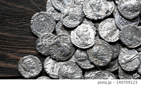 Pile of ancient Roman silver coins on a dark wooden background. Collection of silver denarii featuring portraits of emperors. Historical numismatics and archaeology concept. 140709123