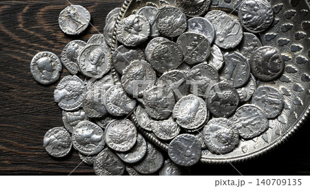 Top view of ancient Roman and Greek silver coins spilling from an ornate metal dish onto a dark wooden table. Historical money collection and antique treasure concept Top view of ancient Roman and Greek silver coins spilling from an ornate metal dish onto a dark wooden table. Historical money collection and antique treasure concept 140709135