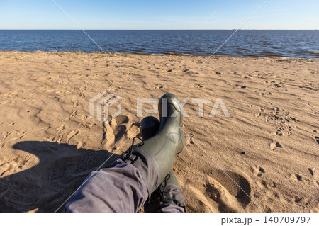 Relaxing on a sandy shore with crossed rubber boots Relaxing on a sandy shore with crossed rubber boots 140709797
