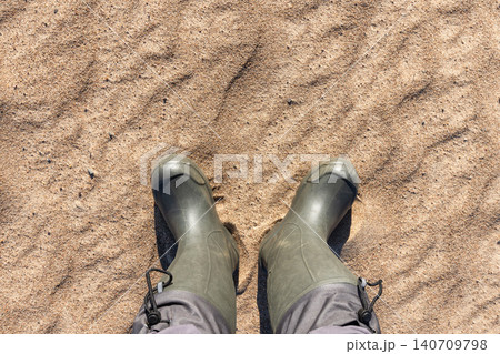 Top-down view of green rubber boots standing on fine sand 140709798