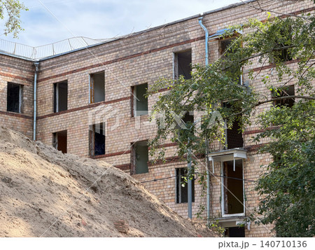 Brick residential building stands beside large sand embankment during redevelopment works, open window frames, exposed structure, transformation of urban housing environment. Construction activity Brick residential building stands beside large sand embankment during redevelopment works, open window frames, exposed structure, transformation of urban housing environment. Construction activity 140710136