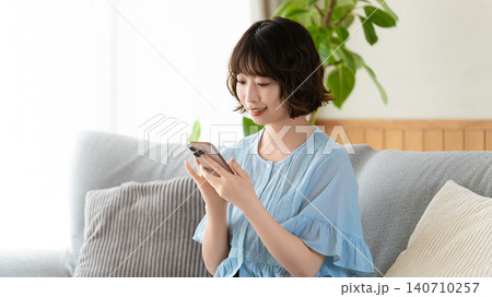 ソファに座ってスマートフォンを使う女性 ソファに座ってスマートフォンを使う女性 140710257