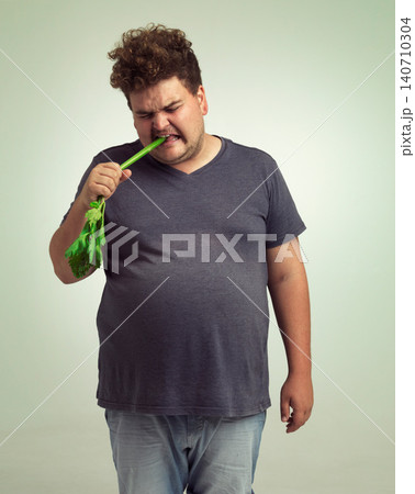 Obesity, weight gain and humor for man in studio with celery for health eating, nutrition and diet. Overweight person with vegetable in mouth and cry for hungry, and food with vitamin for comic 140710304