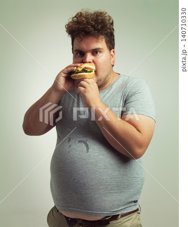 Burger, plus size and portrait for man in studio with diet for unhealthy eating, hungry and greed. Young person with meal in mouth and round stomach for messy eater, calories and takeaway indoor Burger, plus size and portrait for man in studio with diet for unhealthy eating, hungry and greed. Young person with meal in mouth and round stomach for messy eater, calories and takeaway indoor 140710330
