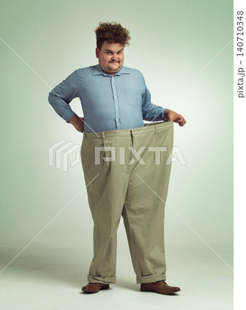 Happy man, portrait and plus size with pants for waist, weight loss or measurement on a studio background. Male person with smile for healthy diet, obesity or overweight clothing on mockup space 140710348