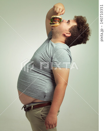 Fast food, hungry and man with hamburger in studio background with lunch, snack and craving for plus size guy. Male person, burger and takeaway for meal in mouth for eating, starving and bite Fast food, hungry and man with hamburger in studio background with lunch, snack and craving for plus size guy. Male person, burger and takeaway for meal in mouth for eating, starving and bite 140710351