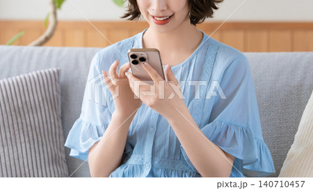 リビングのソファに座ってスマートフォンを使う女性 リビングのソファに座ってスマートフォンを使う女性 140710457