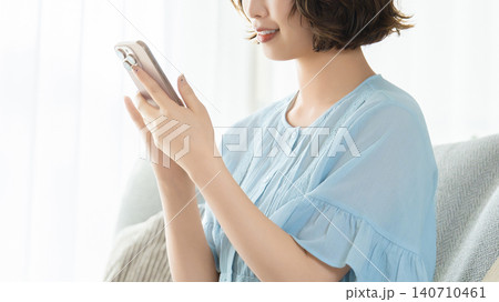 リビングのソファに座ってスマートフォンを使う女性 リビングのソファに座ってスマートフォンを使う女性 140710461