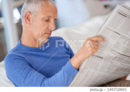 Senior, man and reading a newspaper on sofa for article, information and morning routine in living room of home. Elderly, person and media paper for global news, knowledge or relax on couch in lounge 140710601