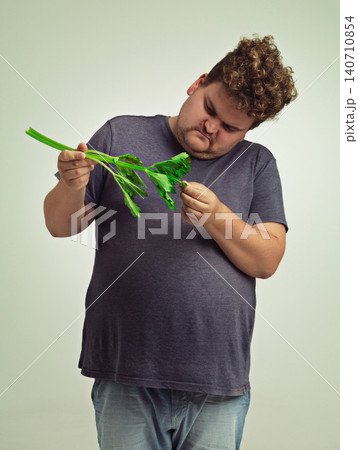 Plus size, diet and unhappy man with vegetable for health benefits, nutrition and wellness in studio in white background. Weight loss, celery and male person for healthy food, wellbeing and detox 140710854