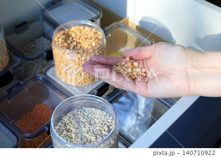 Yellow split peas in woman hand over kitchen drawer storage, plastic containers with dry grains and groats close up Yellow split peas in woman hand over kitchen drawer storage, plastic containers with dry grains and groats close up 140710922