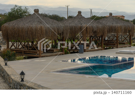 Relaxation huts near a sparkling pool surrounded by tranquil nature at dusk Relaxation huts near a sparkling pool surrounded by tranquil nature at dusk 140711160