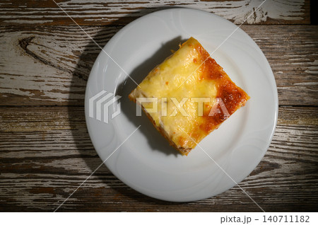 Deliciously baked cheese lasagna served on a rustic wooden table during a cozy evening gathering Deliciously baked cheese lasagna served on a rustic wooden table during a cozy evening gathering 140711182