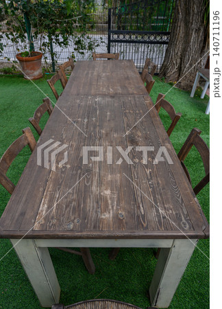 Long wooden table surrounded by chairs under lush greenery in a peaceful outdoor 140711196