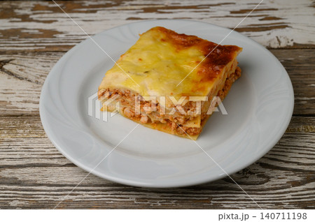 Delicious layers of cheesy lasagna served on a bright white plate against a rustic wooden background Delicious layers of cheesy lasagna served on a bright white plate against a rustic wooden background 140711198