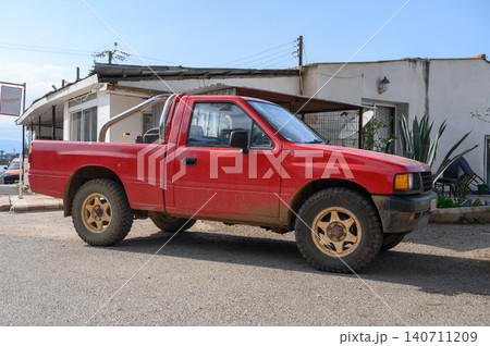 Red pickup truck parked in a dusty street near a rustic building under a clear blue sky Red pickup truck parked in a dusty street near a rustic building under a clear blue sky 140711209
