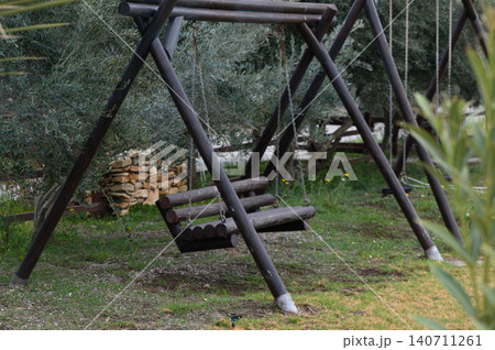 Rustic wooden swing sways gently among the olive trees in a serene garden under soft afternoon light Rustic wooden swing sways gently among the olive trees in a serene garden under soft afternoon light 140711261