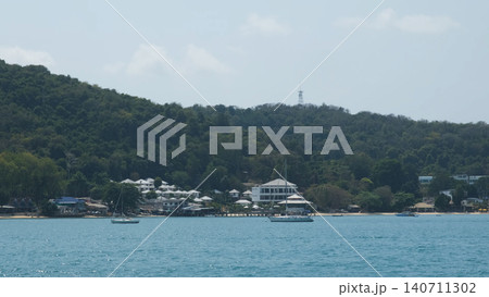 Panoramic view of Samet Island green hillside with buildings and calm turquoise sea in foreground from a ferry. Island scenery concept 140711302
