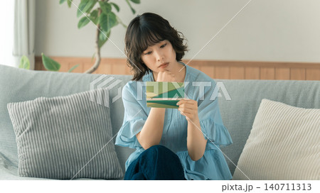 通帳を見て考える女性 通帳を見て考える女性 140711313