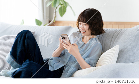 リビングのソファに座ってスマートフォンを使う女性 リビングのソファに座ってスマートフォンを使う女性 140711316