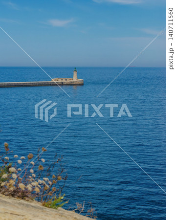 St Elmo Breakwater Lighthouse at Valletta Grand Harbour entrance Malta with deep blue Mediterranean sea and wildflowers foreground St Elmo Breakwater Lighthouse at Valletta Grand Harbour entrance Malta with deep blue Mediterranean sea and wildflowers foreground 140711560