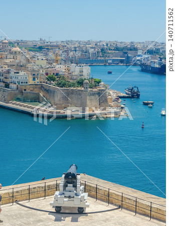 Historic cannon at Saluting Battery overlooking Grand Harbour Valletta Malta with Three Cities fortifications ships and blue sea Historic cannon at Saluting Battery overlooking Grand Harbour Valletta Malta with Three Cities fortifications ships and blue sea 140711562