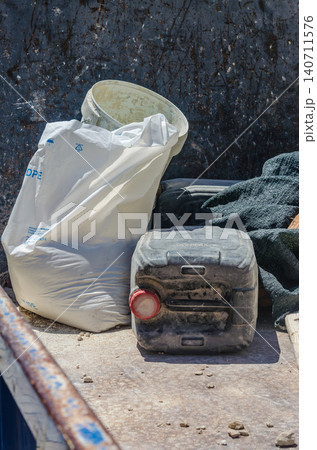 White plastic bag bucket and dirty black jerrycan container on construction site with rusty metal and stones in bright sunlight White plastic bag bucket and dirty black jerrycan container on construction site with rusty metal and stones in bright sunlight 140711576