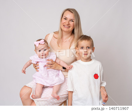 Close-up studio portrait of a radiant blonde mother, her preteen son, and her adorable infant daughter. All three are looking directly into the camera with bright, genuine smiles. Beautiful family of Close-up studio portrait of a radiant blonde mother, her preteen son, and her adorable infant daughter. All three are looking directly into the camera with bright, genuine smiles. Beautiful family of 140711907
