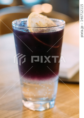 Lavender drink. Refreshing shot. Ice alcohol cocktail with clear bottom dark violet top garnished with lemon slice on wood counter. Lavender drink. Refreshing shot. Ice alcohol cocktail with clear bottom dark violet top garnished with lemon slice on wood counter. 140712115
