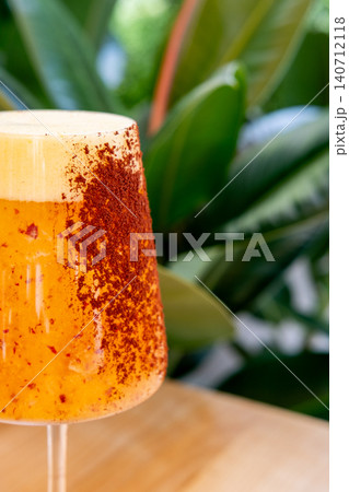 Tropical orange drink. Citrus beverage. Fresh cocktail with cream in glass on table with green exotic leaves garnished with spicy fruit. Tropical orange drink. Citrus beverage. Fresh cocktail with cream in glass on table with green exotic leaves garnished with spicy fruit. 140712118