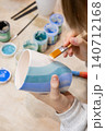 Ceramic art. Pottery class. Unrecognizable talented child hand painting on cup using brush developing creative skill in artisan workshop. 140712168