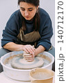 Ceramic artist working. Pottery manufacturing. Professional woman artisan shaping raw material forming clay on wheel interior. 140712170