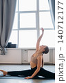 Fitness activity. Yoga exercise. Young female athlete in split pose raising arm stretching in studio. Body sport therapy practicing indoors. 140712177