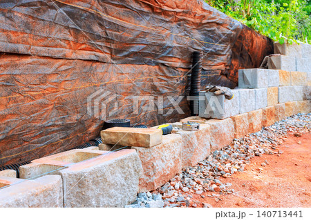 Cement blocks are laid out along dirt path with tools nearby at construction site during retaining wall install 140713441
