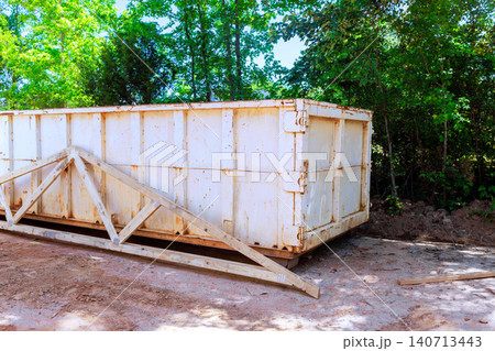 Large white container sits at construction site surrounded by trees, collecting debris waste Large white container sits at construction site surrounded by trees, collecting debris waste 140713443