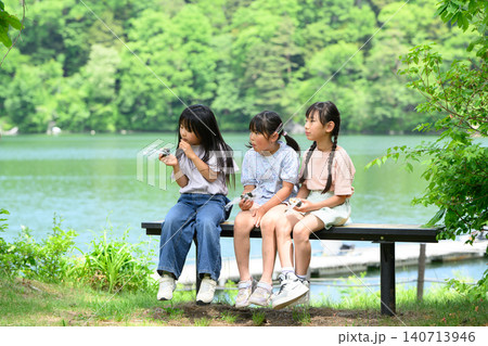 新緑の湖畔のベンチで仲良くおにぎりを食べる女子小学生たち	 140713946
