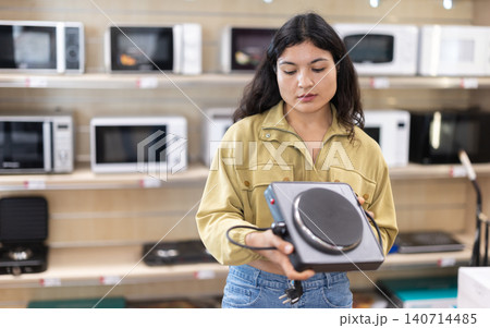 Young woman choosing portable electric cooktop at household appliances store Young woman choosing portable electric cooktop at household appliances store 140714485
