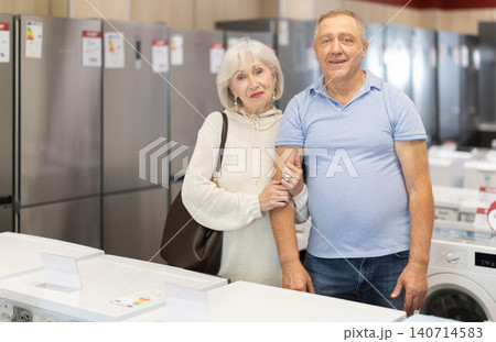 Visiting store mature couple is looking at something on shelf of showcase Visiting store mature couple is looking at something on shelf of showcase 140714583