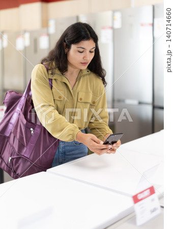 Young woman scanning QR-code on dishwasher at household appliances store 140714660