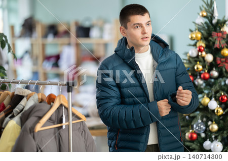 Guy customer is trying on down jacket in store, X mas Eve Guy customer is trying on down jacket in store, X mas Eve 140714800
