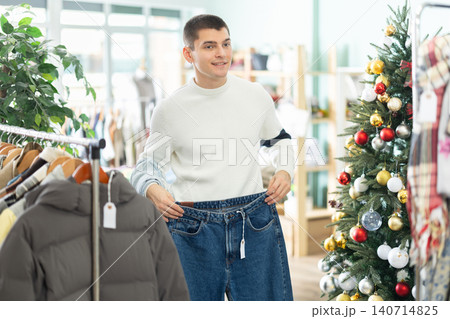 Guy client pre-examine fabric and style of product, is busy choosing jeans, X mas discount. Guy client pre-examine fabric and style of product, is busy choosing jeans, X mas discount. 140714825
