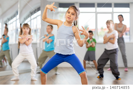 Positive juvenile girl engaged in breakdancing in training room with children's group Positive juvenile girl engaged in breakdancing in training room with children's group 140714855