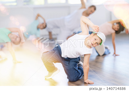 Expressive cheerful teen boy practicing hip-hop movements on floor during group dance class with teacher in studio Expressive cheerful teen boy practicing hip-hop movements on floor during group dance class with teacher in studio 140714886