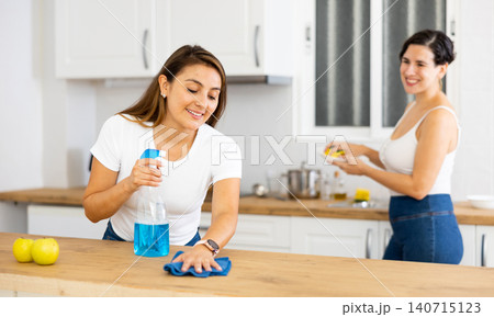 Woman cleaning countertop in kitchen while friend washes dishes 140715123