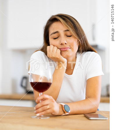 Young depressed Latina with glass of wine and silent phone in kitchen Young depressed Latina with glass of wine and silent phone in kitchen 140715146